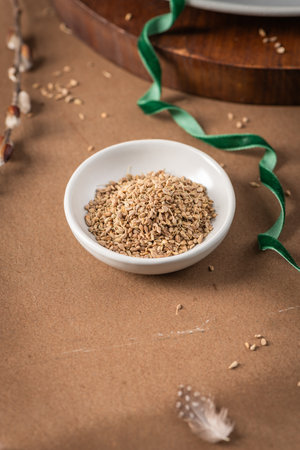 Fennel seeds in a white bowl on a textured brown surface with a delicate feather in the backgroundの写真素材