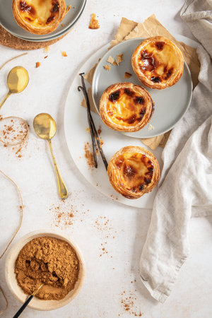 A collection of Pastel de Nata, traditional Portuguese custard tarts, are arranged on plates with...