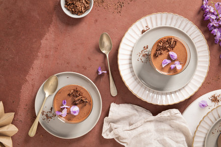An overhead view shows two creamy chocolate mousses in glasses, styled with spoons, garnishes, and decorations on a textured surface, inviting treat.の写真素材