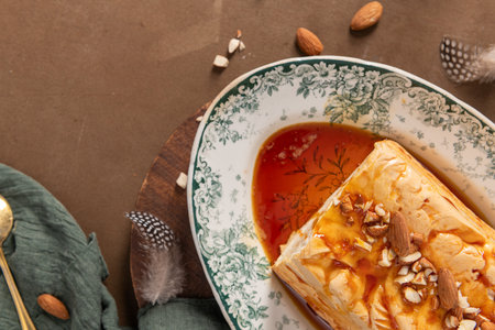 A slightly angled overhead shot features a piece of traditional caramelized egg white pudding known as molotof, generously covered in syrup and chopped almonds, served on a decorative plateの写真素材