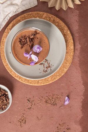 An overhead view captures a single creamy chocolate mousse in a glass, styled on plates with a cork placemat, bowl of shavings, and decorative paper fan.の写真素材