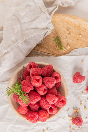 An overhead shot of a rustic ceramic bowl filled with fresh raspberries and scattered granola on a...
