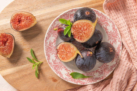 A close-up, top-down view of whole and halved figs on a decorative plate and a wooden board with...