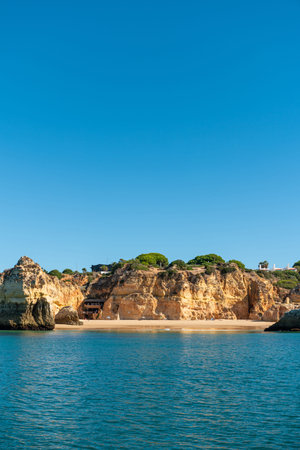 Algarve beach cove framed by golden cliffs and turquoise Atlantic water under a brilliant blue sky,...