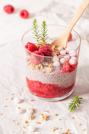 A single glass of layered raspberry and chia seed pudding topped with fresh raspberries on a rustic white tableの写真素材