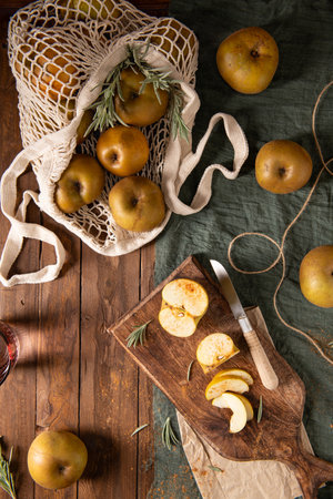 An overhead shot of a rustic still life with russet apples, some in a string bag, with others sliced and sprinkled with cinnamon, on a wooden tableの写真素材