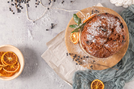 Overhead flat lay of a sugar-dusted panettone on a wooden board, decorated with dried oranges, holly, and berries on a light gray holiday backdropの写真素材