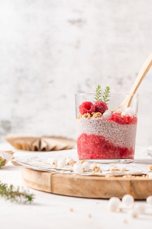 A single glass of layered raspberry and chia seed pudding topped with fresh raspberries on a rustic wooden platterの写真素材