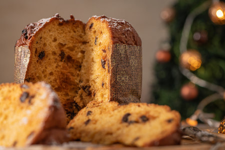 A delicious, moist Panettone, partially sliced to show the interior with raisins and dusted with sugar, against a cozy Christmas tree background with soft bokeh lightsの写真素材
