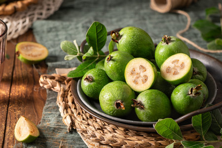 A rustic still life with ripe pineapple guavas, some cut open to reveal the fleshy pulp, on a small plate and in a basketの写真素材