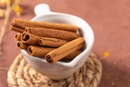 A selection of fragrant cinnamon sticks arranged in a white ceramic bowl sitting on a woven jute...
