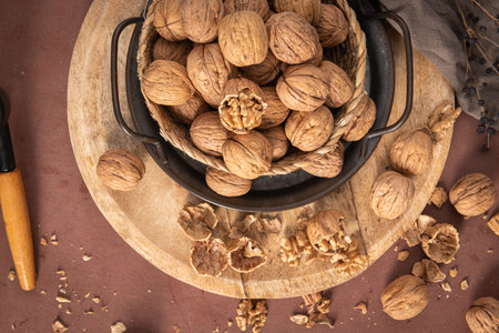 A high-angle shot showcasing a wicker basket filled with whole walnuts sitting on a round wooden...