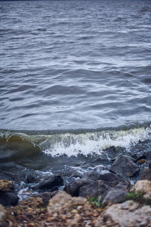 Small wave on the stone shore. Sea or lake with dark water. Wild Nature Dramatic Background