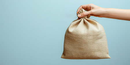 A hand holds a burlap sack against a blue background.の素材