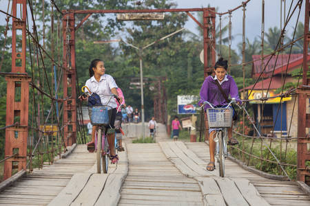 VANG VIENG, LAOS - 7 December 2012: Young unidentified girl cycling back from school on a Wooden Bridge.のeditorial素材