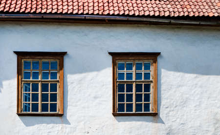 Old wooden Windows of the house. Two Windows on a white wall under the roof of . The sun shines brightly. Estonia.の写真素材