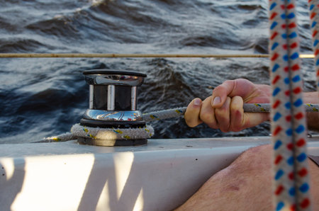 Handsome man working on sailboat, pulling rope, active summer vacation on water transport, having fun in the sea, enjoying water sport.の写真素材