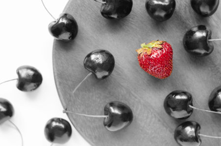 The concept of differences in society. One is different from the others. One against all. Fresh berry. Strawberries and cherries. The view from the top. Metaphor. Black and white concept.の写真素材