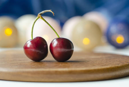 Ripe cherry close-up. Two berries on one branch. Cherry sisters. Blue blurred background. Bokeh. Garlands are burning. Wooden substrate.の写真素材