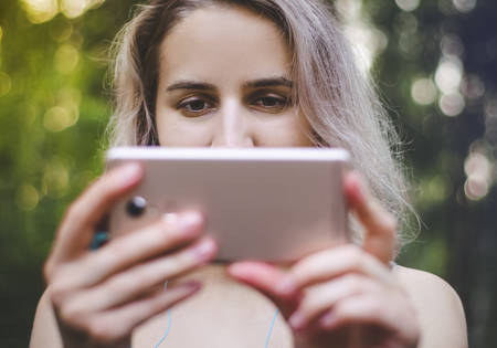 The girl is watching a video on the phone. Film, series. Internet. Blonde woman in sports clothes. Emotions. Photo. The glare of the sun.の写真素材