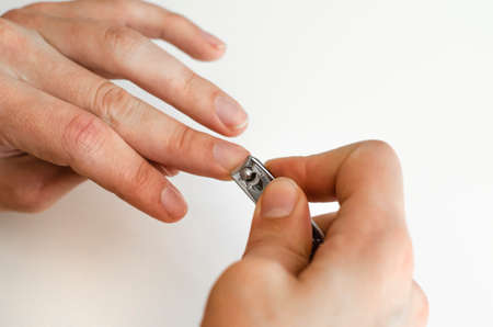 A young man does a manicure to himself. On white background. Hands. Stages of nail clipping. Close up.の写真素材