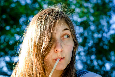 Beautiful young girl drinking a drink from a tube. He looks away in surprise. Bokeh in the background, summer.の写真素材