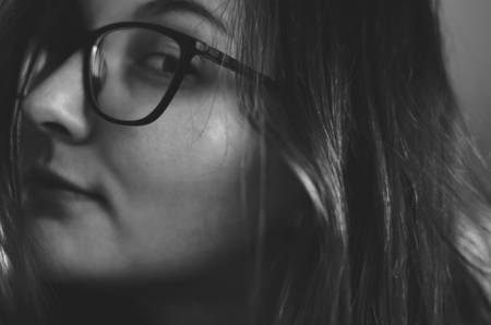 Portrait of a young beautiful girl with glasses. Mysterious art photography. The girl looks at the frame. Black and white photo.の写真素材