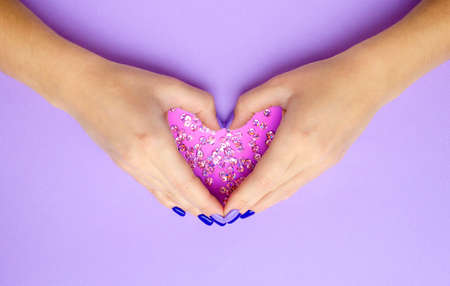 Girl holding hands with heart. Stylish trendy women's manicure. Care. Female hand. Lilac background with sequins.の写真素材