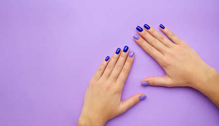 Stylish trendy women's manicure. Blue and lilac color gel Polish. The view from the top. Care. Female hand. Lilac background.の写真素材