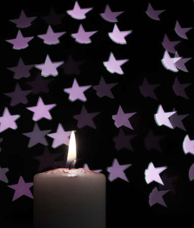 Abstract - burning candle with blur violet stars on black backgroundの写真素材