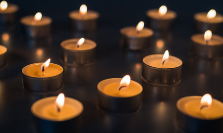 Flame of many candles burning on the background in dark brown and yellow color - sadness