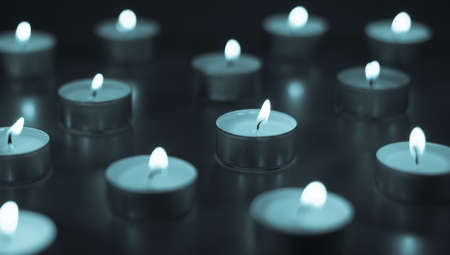 Flame of many candles burning on the background in blue and white colorの写真素材