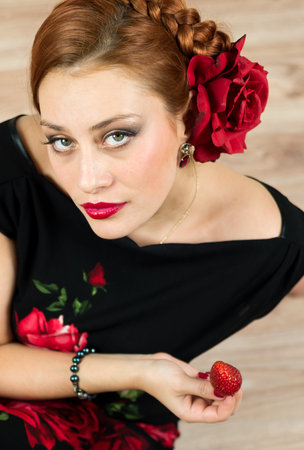 Woman with red flower and black dress eating strawberry