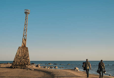people walking along the seaside with old lighthouseの写真素材