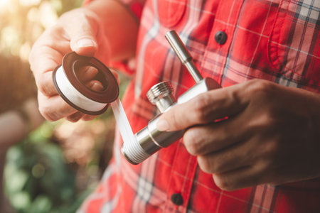 Asian Man Plumber in Plaid shirt winds seal tape on a thread of a plumbing fitting, two hands...