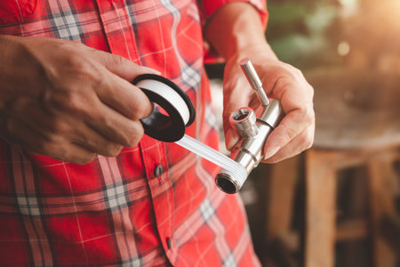 Asian Man Plumber in Plaid shirt winds seal tape on a thread of a plumbing fitting, two hands wrapped water tap or faucet for Connect the pipe, Close-upの写真素材