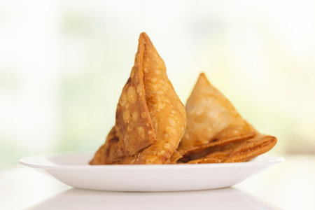 Fried samosas on white plate on green background, closeup