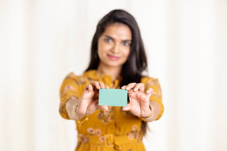 Young indian woman holding a blank business card. Focus on cardの写真素材