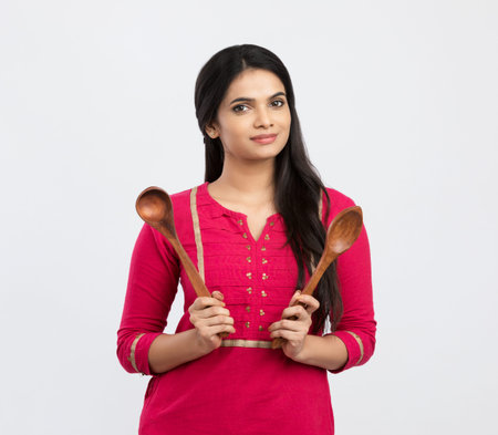 Young indian woman holding kitchen utensils over white background.