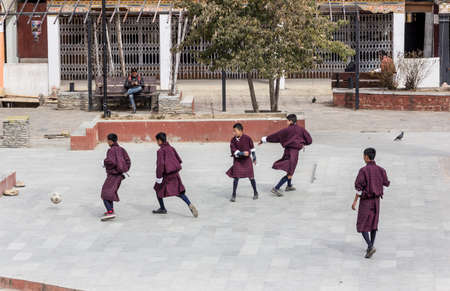 Bhutanese school boys in traditional costumes playing soccer in the street のeditorial素材