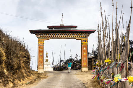A tourist is taking a photograph of the gate and prayer flags at Yotong La pass at a height of 3300 m  Bhutan  In the background is a choerten   unrecognizable person の写真素材