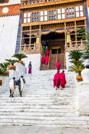 The stairs go steeply up to the dzong of Punakha, Bhutan. Monks and unrecognizable people in traditional costumes are climbing the stairs. Dzongs are fortress like buildings which house a monastery and administrative offices. (faces blurred)のeditorial素材