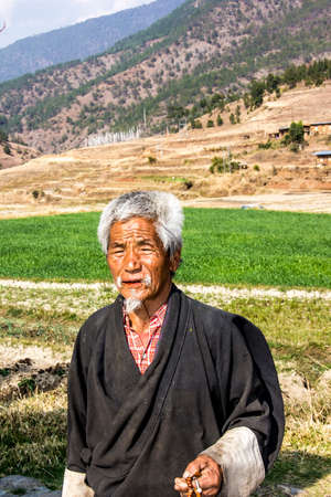 A bhutanese farmer is standing in front of his green rice fields  In the background are prayer flags のeditorial素材