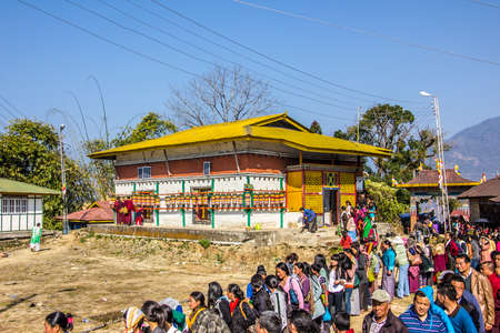 At the bumchu festival, Tashiding, Sikkim, Buddhist believers, men and women,  are queuing in two lines to get into the temple  In the back is a beautiful temple with many prayer wheels のeditorial素材