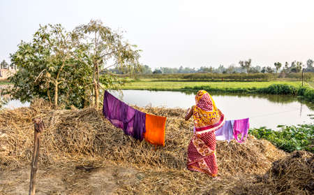 A nepali woman in a colorful saree is hangig up her laundry in the countryside of the terai, the most southern, warm, flat and fertile part of Nepal   unrecognizable person のeditorial素材