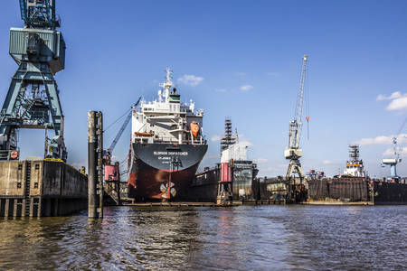 A big containership is lying in the drydock, in the harbor of Hamburg, Germany. Cranes and other industrial machinery is around.のeditorial素材