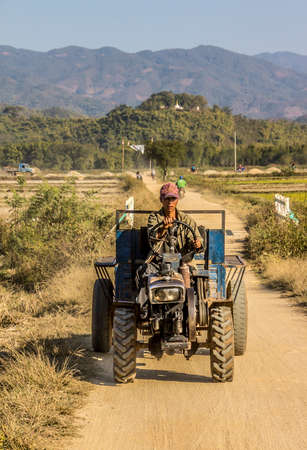 A farmer is driving a tractor near keng Tung, Myanmar. In the background is a paya or pagoda on a hill.のeditorial素材