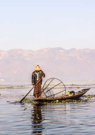 A fisherman at Inle lake iscatching fish in a big fish trap. In the background are the moutainsのeditorial素材