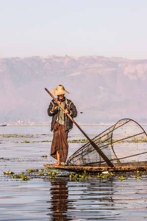 A fisherman at Inle lake iscatching fish in a big fish trap. In the background are the moutainsのeditorial素材