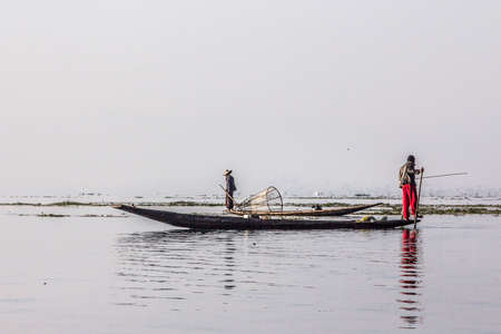 A fisherman at Inle lake iscatching fish in a big fish trap. In the background are other fishermenのeditorial素材